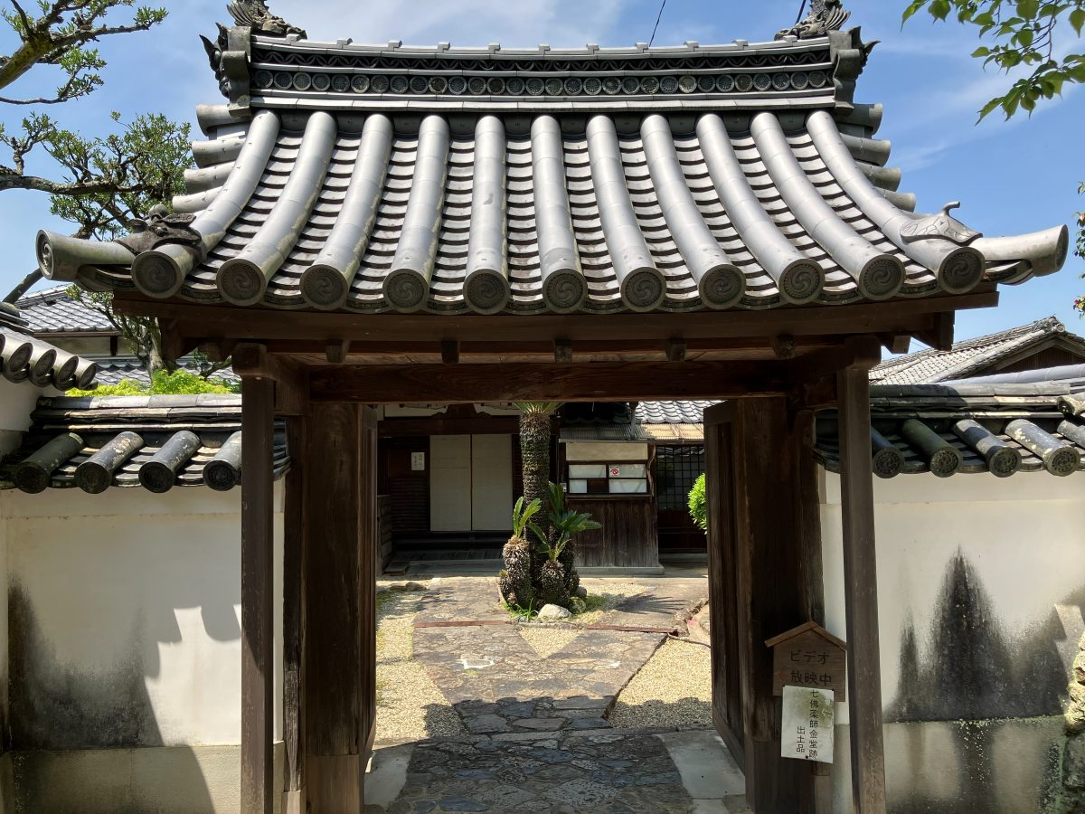 The other garden entrance — a tiled-roof gate with signs for the video screening and excavated objects