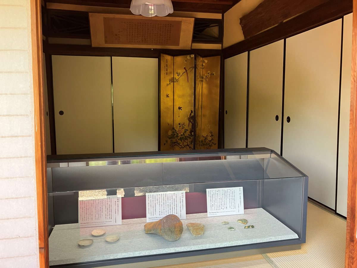 A display case at Shin-Yakushiji with oil-lamp dishes, a round eaves tile and Nara three-colour ware excavated from the old grounds